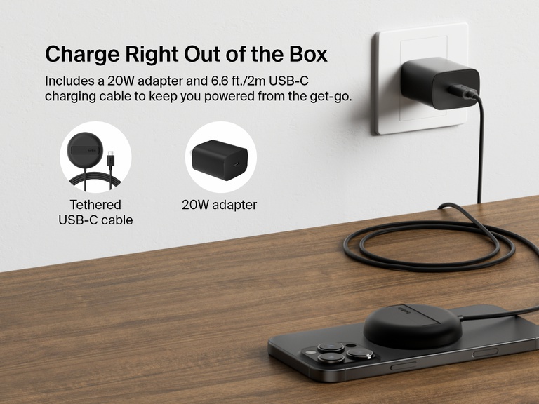 A black Belkin BoostCharge Pro Magnetic Wireless Charging Pad with Qi2 15W is shown charging an iPhone on a desk, highlighting its included 20W power adapter and 6.6ft/2m tethered USB-C cable for out-of-the-box convenience.