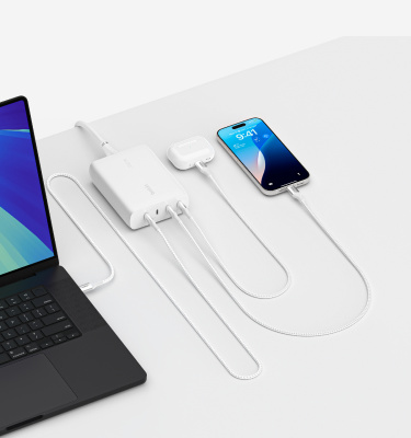 Fast charging setup displaying a laptop, smartphone, and wireless earbud case connected to a multi-port USB-C charger. All devices are charging simultaneously on a clean, white surface, highlighting efficient charging for multiple devices.