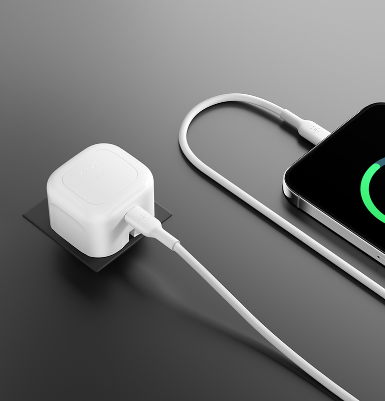 The image shows the Belkin BoostCharge Compact USB-C Wall Charger 30W with foldable prongs placed in a suitcase alongside a passport and a camera, highlighting its compact, travel-friendly design.