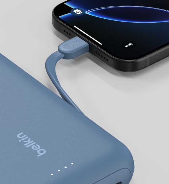 A close-up of a blue Belkin BoostCharge Power Bank 20K with Integrated Cable connected to a smartphone, showing the "in/out" label on the cable and LED indicator lights on the power bank. A close-up of a blue Belkin BoostCharge Power Bank 20K with Integrated Cable connected to a smartphone, showing the "in/out" label on the cable and LED indicator lights on the power bank.