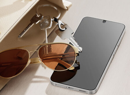 Smartphone resting on a tabletop beside keys and sunglasses, with a matte-looking screen surface that suggests reduced glare and scratch resistance.