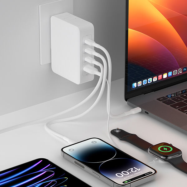 A white multi-port wall charger plugged into a wall outlet, with four white charging cables extending to power various devices, including a MacBook, an iPhone, an iPad, and an Apple Watch on a charging pad. The setup is arranged neatly on a white desk, showcasing a clean and organized workspace.