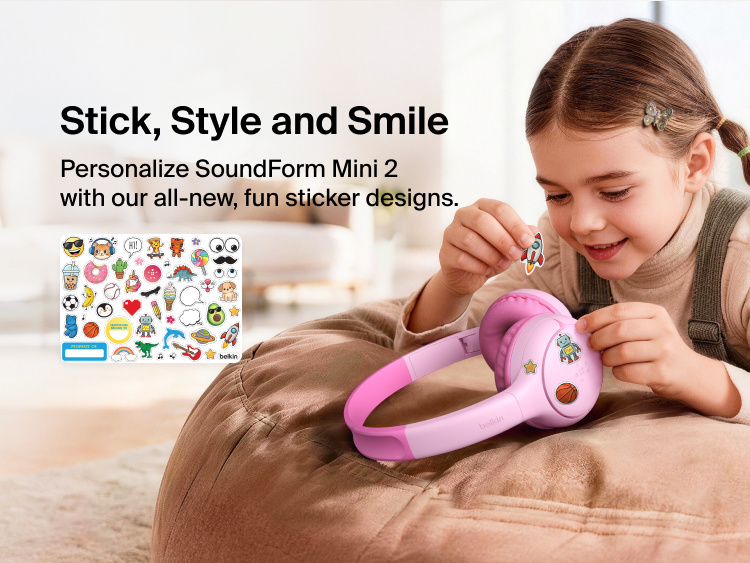 Child applying decorative stickers to the SoundForm Mini 2 Wireless On-Ear Headphones for Kids, with a full sticker sheet visible featuring playful emoji-style designs and a name label