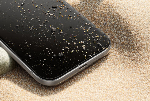 강화유리가 부착된 스마트폰을 모래 위에 올려놓은 모습. 화면에 작은 돌과 알갱이가 흩어져 있습니다.