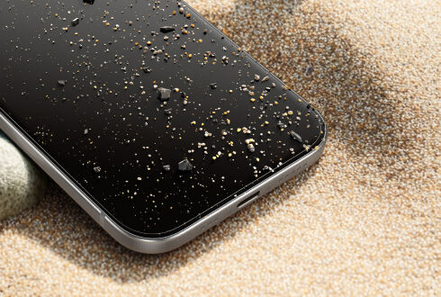 Close-up of a smartphone with a screen protector, lying on sand with small rocks and grains scattered on the display. Close-up of a smartphone with a screen protector, lying on sand with small rocks and grains scattered on the display.