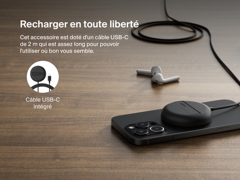 Image montrant la station de recharge sans fil noire Belkin BoostCharge Pro avec Qi2 (15 W) posée sur un surface plane en bois, qui recharge un iPhone et qui met en avant son câble USB-C intégré (2 m).
