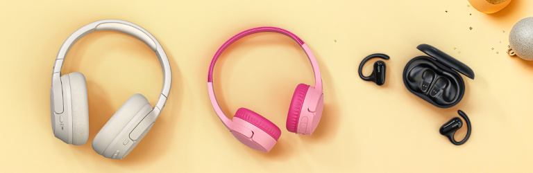 Holiday banner featuring Belkin audio gifts on a festive gold background, including white and pink over-ear headphones, and black wireless earbuds with a charging case, surrounded by ornaments, stars, and wrapped presents.
