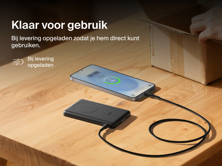 Belkin BoostCharge Slim Magnetic Power Bank 5K shown charging a smartphone on a table, highlighting its precharged battery ready for instant use out of the box.