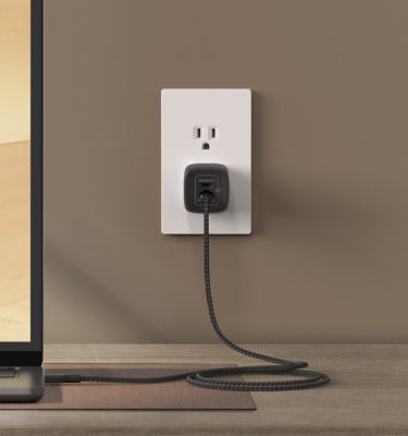 Belkin Fast-Charging USB-C Cable and GaN Charger Bundle plugged into a wall outlet powers a laptop efficiently on a modern desk setup.