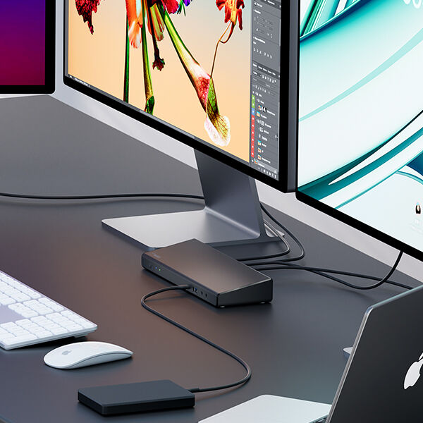 A professional workstation setup featuring dual monitors displaying creative digital work, a laptop, and a Belkin docking station. Various peripherals, including a keyboard, mouse, and external storage drive, are connected, ensuring seamless multitasking and an efficient workflow. Cables are neatly managed for a clean desk appearance.