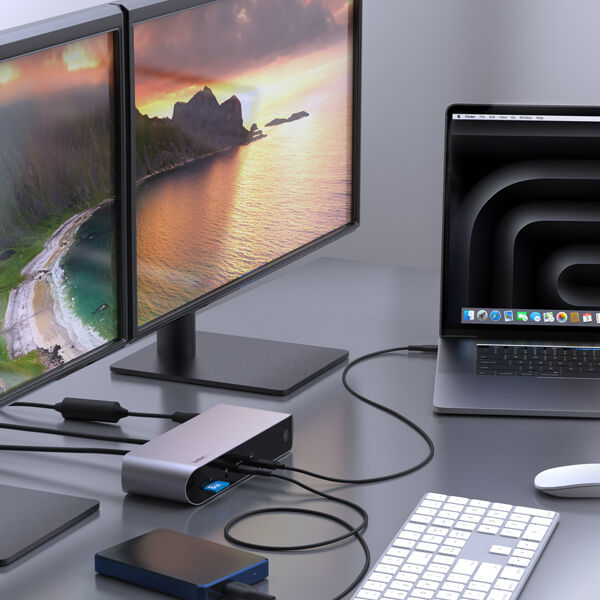 A Belkin docking station connected to a MacBook and dual monitors, creating a versatile workstation setup. The docking station enables multi-display support, with various cables plugged in for expanded connectivity, including USB peripherals, external storage, and power delivery. The modern workspace features a sleek keyboard, a trackpad, and an external hard drive, emphasizing efficient workflow and productivity.