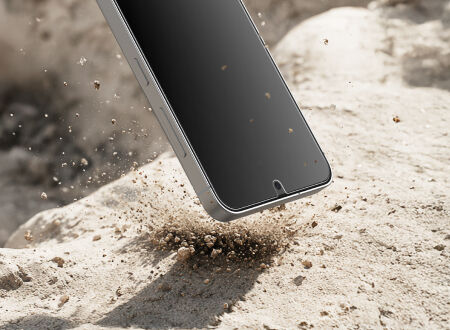 Close-up of a smartphone landing on rough stone, with dust and small rocks scattering to convey shock and impact protection.