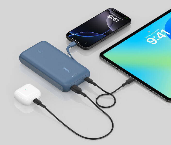 파란색 케이블 일체형 Belkin BoostCharge 보조 배터리 20K가 iPhone, iPad, AirPods을 동시에 충전하는 모습이 거울 같은 표면에 반사됩니다.