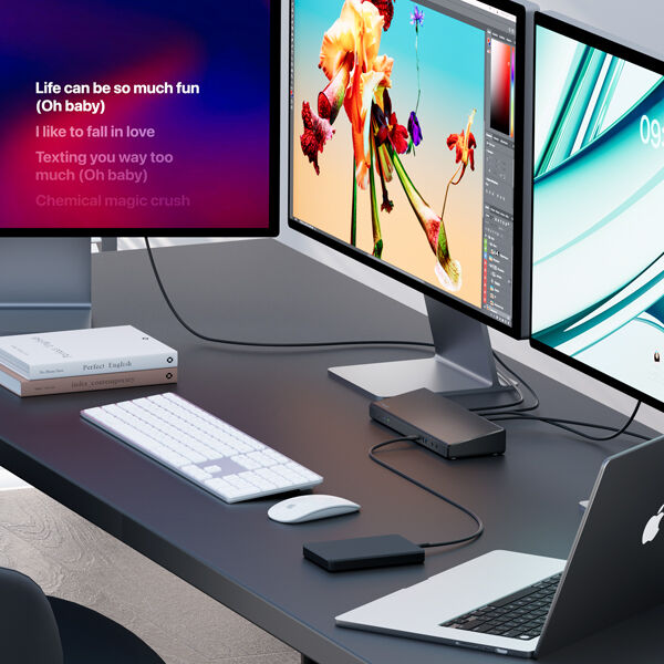 A modern workstation setup featuring a Belkin docking station connected to a MacBook and multiple monitors. The screens display graphic design software, a digital clock, and song lyrics, showcasing a versatile and creative workspace. A wireless keyboard and mouse are placed on the sleek black desk, along with an external hard drive and books, emphasizing productivity and efficiency. The multi-monitor setup is ideal for graphic design, music, and multitasking workflows.