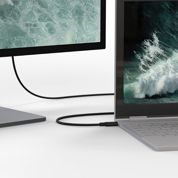 A silver laptop connected to an external monitor via a black cable, displaying the same ocean wave image on both screens. The laptop is in a partially folded position, suggesting it might be a 2-in-1 convertible device. The clean white background emphasizes the minimalist and modern workspace setup.
