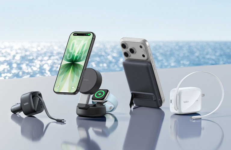Belkin on-the-go charging accessories including car charger, magnetic wireless charging stand with iPhone and Apple Watch, portable power bank, and wall charger displayed on a clean surface with an outdoor water backdrop