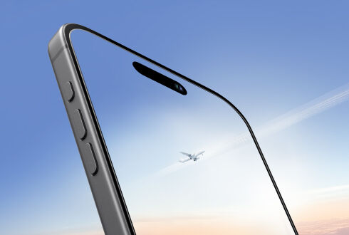 투명한 강화유리를 붙인 스마트폰의 클로즈업 사진. 머리 위로 비행기가 지나가는 하늘이 반사되어 선명함과 투명성을 상징합니다.