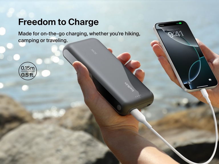 A 0.15m (0.5 ft) Belkin BoostCharge USB-A to USB-C Cable 15W connects a power bank to a smartphone outdoors, ideal for compact, on-the-go charging while hiking or traveling.