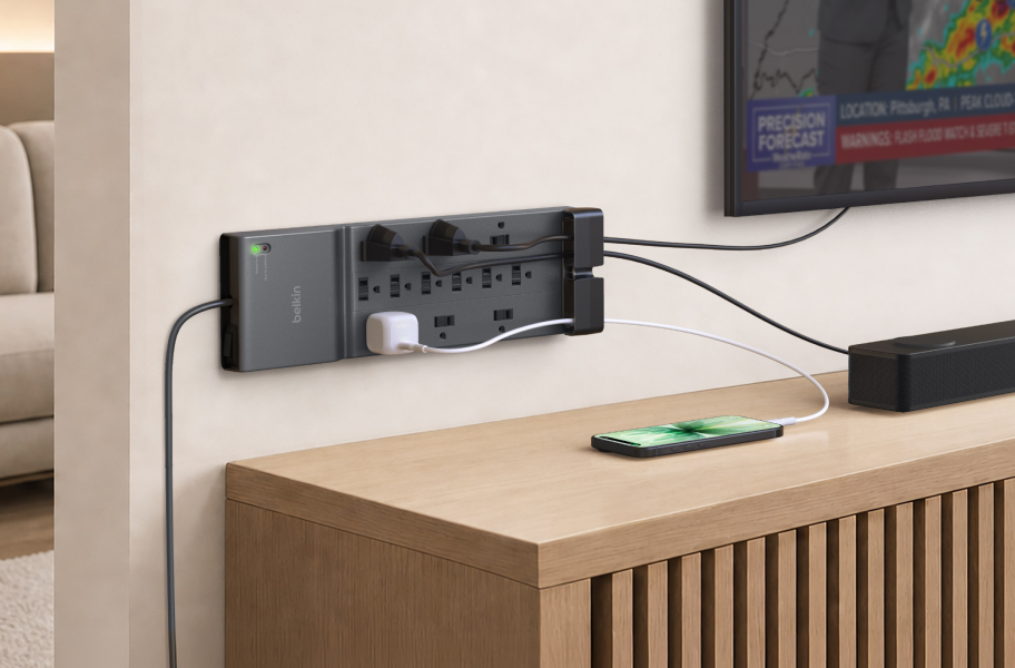 Belkin 12-Outlet Home/Office Surge Protector mounted on a wall, powering a TV, soundbar, and smartphone to provide reliable surge protection for home entertainment devices.