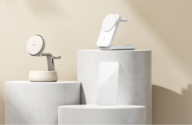 Minimalist product display with Belkin accessories on white marble pedestals, including a beige magnetic charging stand, a white wireless charging dock, and a clear screen protector. Minimalist product display with Belkin accessories on white marble pedestals, including a beige magnetic charging stand, a white wireless charging dock, and a clear screen protector.