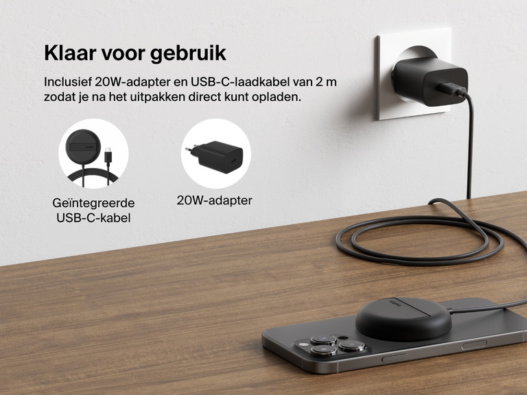 Afbeelding van een zwart Belkin BoostCharge Pro magnetisch draadloos laadstation met Qi2 (15 W) die een iPhone oplaadt op een bureau, waarmee de meegeleverde 20W-voedingsadapter en de vaste USB-C-voedingskabel voor direct gebruik geïllustreerd worden.