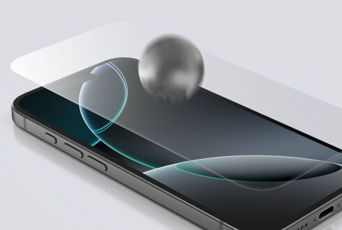 투명한 강화유리가 부착된 스마트폰의 클로즈업 사진으로, 내구성과 충격 저항성을 보여주기 위해 금속 공이 화면에 충돌하는 모습이 담겨 있습니다.