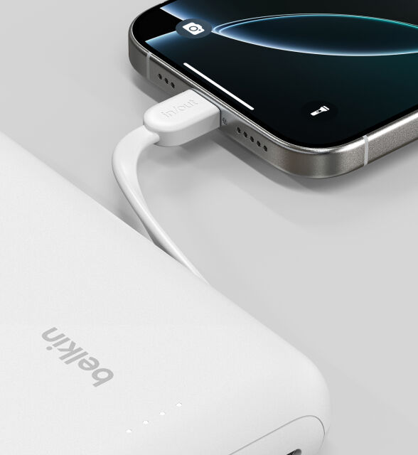 A close-up of a white Belkin BoostCharge Power Bank 20K with Integrated Cable connected to a smartphone, showing the "in/out" label on the cable and LED indicator lights on the power bank. A close-up of a white Belkin BoostCharge Power Bank 20K with Integrated Cable connected to a smartphone, showing the "in/out" label on the cable and LED indicator lights on the power bank.