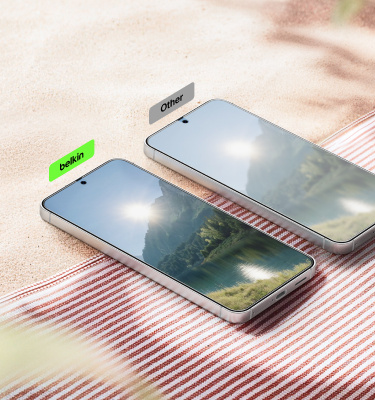 Two smartphones lying on a round marble table in sunlight, one labeled &lsquo;belkin&rsquo; and the other &lsquo;Other,&rsquo; showing a comparison of screen glare and reflections.