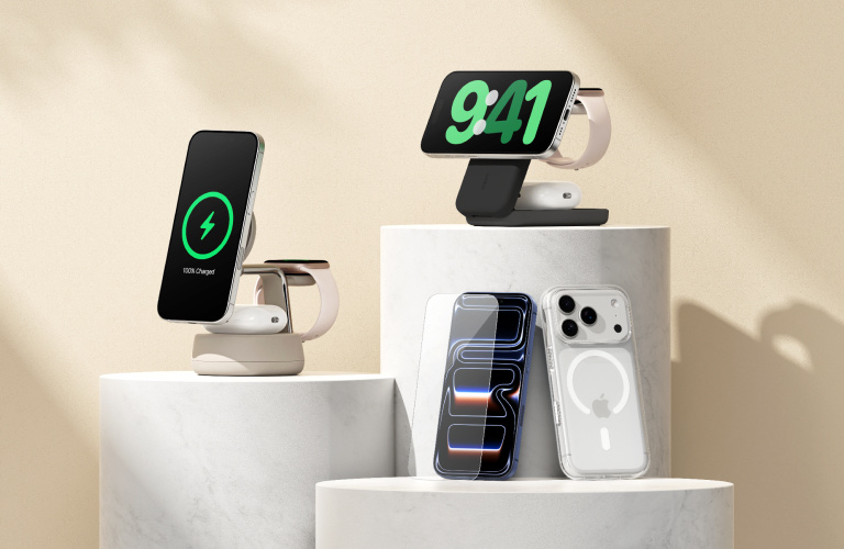 Minimalist product display with Belkin accessories on white marble pedestals, including a beige magnetic charging stand, a white wireless charging dock, and a clear screen protector.