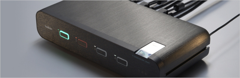 A sleek, black IsoClave RED/BLACK Secure KVM switch with illuminated buttons, connected to multiple cables, designed for secure computer access.