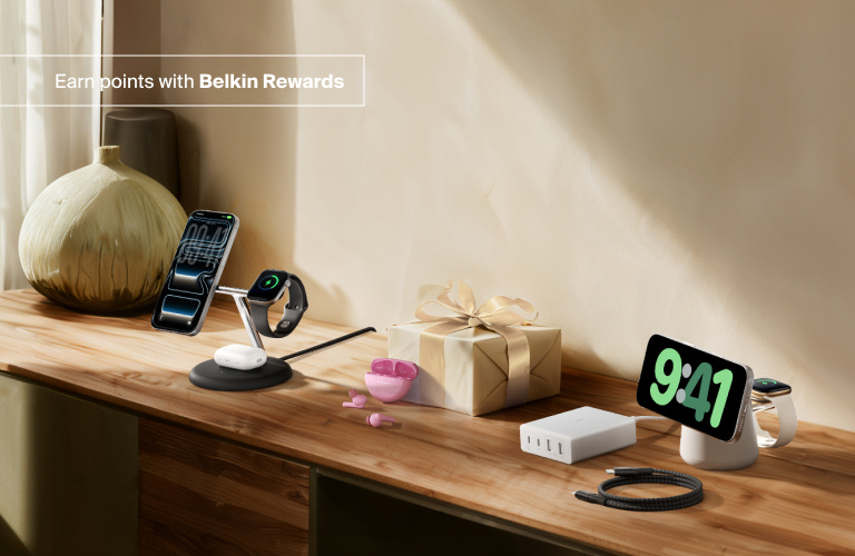Lifestyle setup featuring Belkin wireless charging stands, wall charger, and braided cable on a wooden surface beside a wrapped gift, with the text “Earn points with Belkin Rewards."