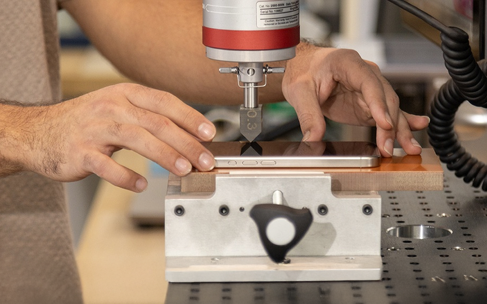 Close-up of a person testing a smartphone’s durability using precision lab equipment that applies pressure to the screen.