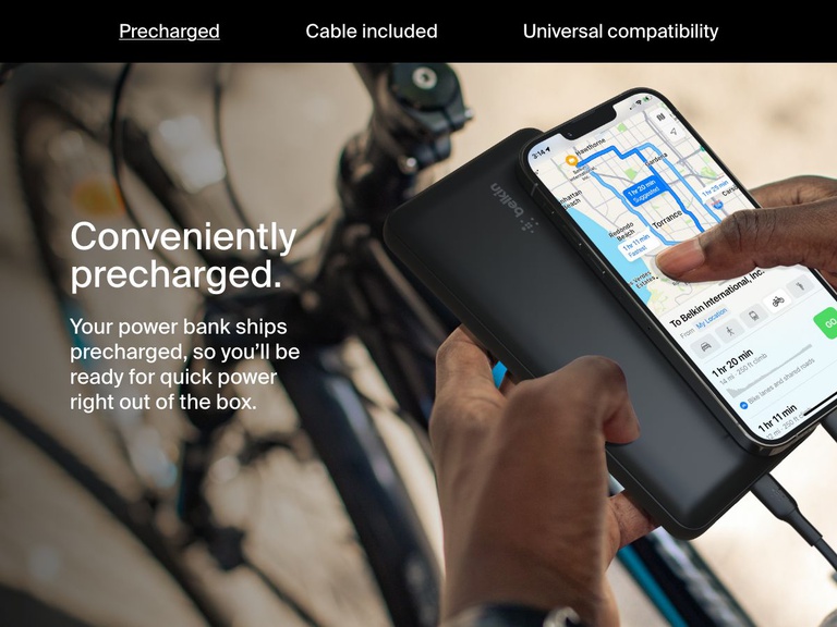 A person charges their smartphone using a black Belkin BoostCharge Power Bank 20K while navigating on a bike, highlighting its convenient precharged feature for immediate use.