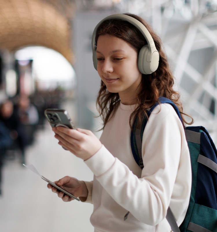 Image rapprochée d'une main tenant un casque audio beige plié avec un arrière-plan flou qui comprend une personne assise au loin.
