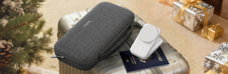 Holiday banner showing Belkin travel tech gifts on a suitcase beside a Christmas tree, including a gray carrying case, a white charging accessory, and a passport, with wrapped presents in the background.
