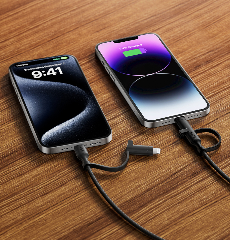 Two iPhones on a wooden surface, both charging via a BoostCharge Pro 2-in-1 Cable with USB-C and Lightning Connector. 