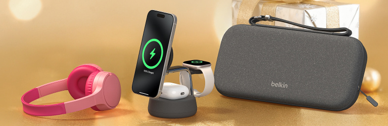 Holiday-themed banner featuring Belkin tech products on a gold background, including pink over-ear headphones, a wireless charging stand holding a phone, smartwatch, and earbuds, and a gray Belkin carrying case, with a wrapped gift in the background.