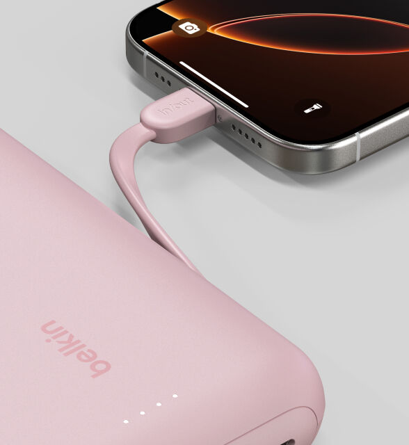 A close-up of a pink Belkin BoostCharge Power Bank 20K with Integrated Cable connected to a smartphone, showing the "in/out" label on the cable and LED indicator lights on the power bank. A close-up of a pink Belkin BoostCharge Power Bank 20K with Integrated Cable connected to a smartphone, showing the "in/out" label on the cable and LED indicator lights on the power bank.