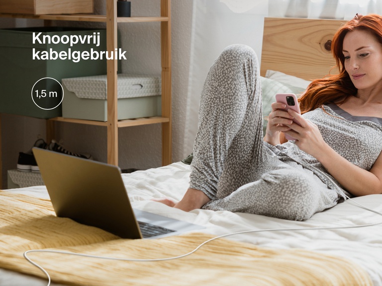 Een vrouw ontspant op bed terwijl ze haar iPhone gebruikt die is verbonden met een Belkin BoostCharge USB-C-kabel met Lightning-connector. De 1,8 meter lange, knoopvrije kabel heeft een praktische lengte voor meer flexibiliteit bij het opladen.