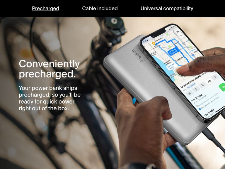 A person charges their smartphone using a silver Belkin BoostCharge Power Bank 20K while navigating on a bike, highlighting its convenient precharged feature for immediate use.