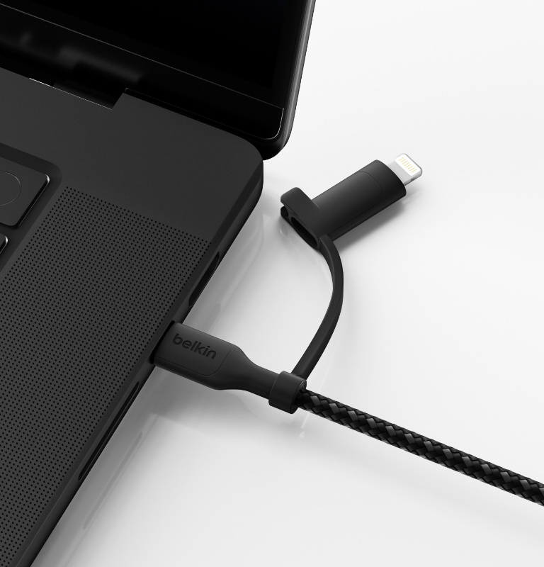A BoostCharge Pro 2-in-1 Cable with USB-C and Lightning Connector is plugged into a laptop on a white surface, with the USB-C connector in use.