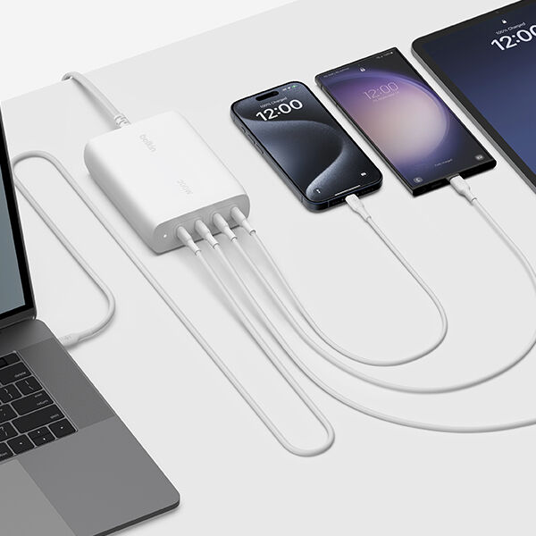 A Belkin charging hub connected to a laptop, charging two smartphones and a tablet via white USB-C cables on a white surface.