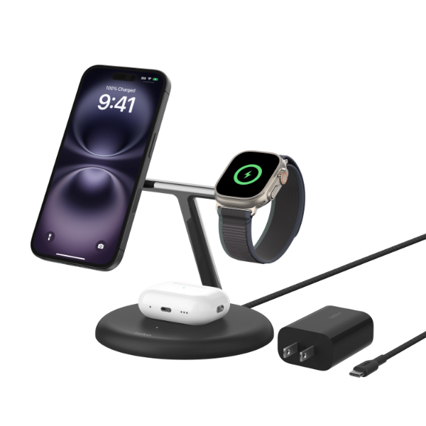 A Belkin 3-in-1 wireless charging stand with an iPhone, Apple Watch, and AirPods charging simultaneously. The stand is black with a sleek, modern design and includes a power adapter and USB-C charging cable.