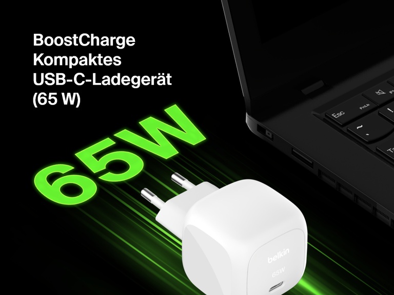 Schrägaufnahme des kompakten Belkin BoostCharge USB-C-Ladegeräts (65 W) neben einem Laptop, auf der seine Fähigkeit zum Schnellladen mit „65W“ in fetten grünen Buchstaben betont wird.