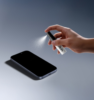 Hand spraying Belkin Titan LiquidGuard solution from a small bottle onto a smartphone lying on a flat surface.
