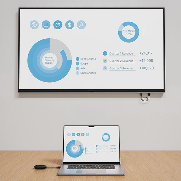 A laptop on a wooden table wirelessly displays a business presentation on a wall-mounted screen. The shared slide shows blue circular charts for market share by region and an 80% profit margin, along with quarterly revenue figures for Q1, Q2, and Q3. The laptop screen mirrors the same graphics.