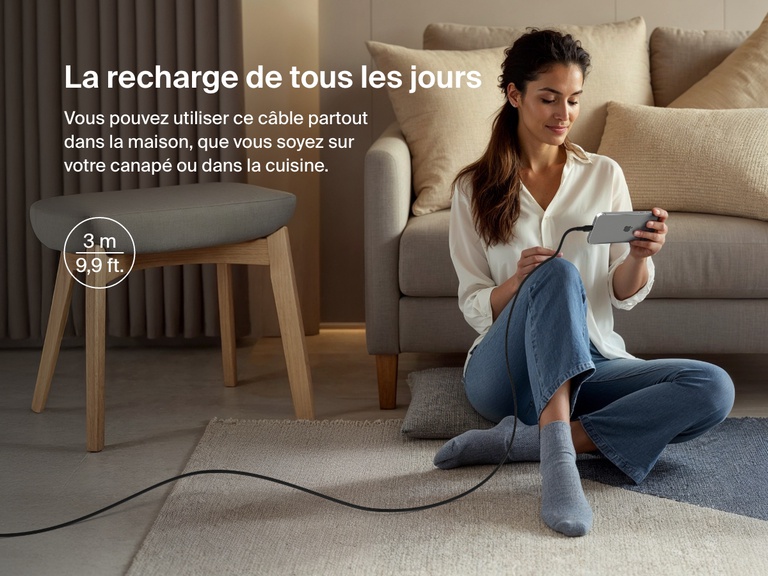 Woman sitting on the floor using a phone connected to the Belkin BoostCharge Pro USB-C to USB-C Braided Cable 240W, shown in a 3-meter (9.9 ft) length for everyday charging flexibility.