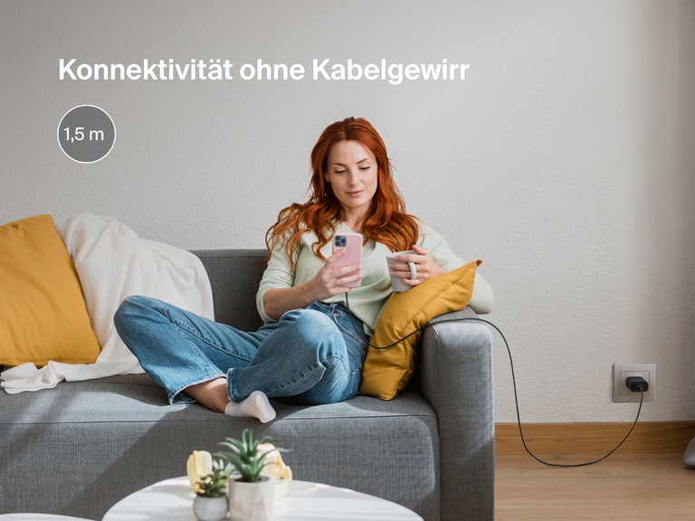 Eine Frau sitzt entspannt mit Ihrem iPhone auf einer Couch. Das iPhone ist mit einem BoostCharge USB-A-Kabel mit Lightning Connector verbunden, das mit einer Länge von 1,8 m eine hohe Reichweite zum Laden hat und sich nicht verheddert.