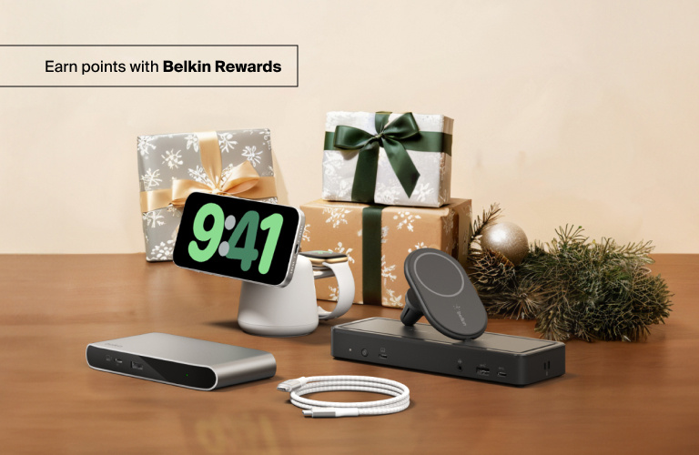 Belkin holiday tech gifts including chargers, docks, and accessories displayed on a wooden surface beside wrapped presents and festive decor.