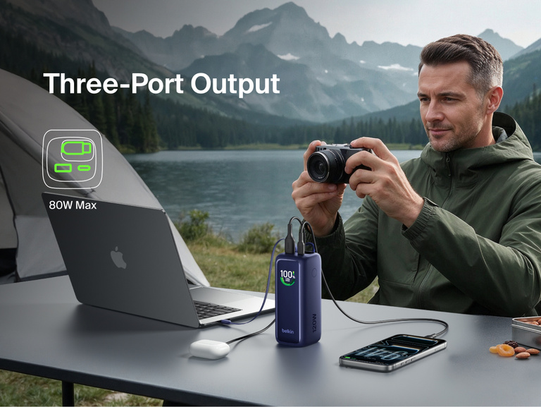 UltraCharge Power Bank 22K with Retractable Cable charging a laptop, camera, and phone at once while camping outdoors, illustrating 80W max three-port output